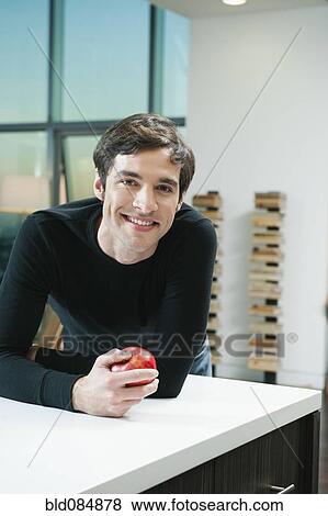 Stock Photo - Caucasian man leaning on counter holding apple. Fotosearch