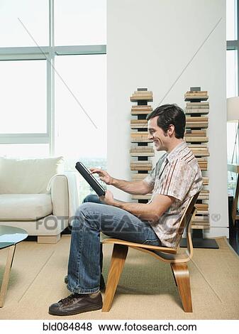 Stock Photo - Caucasian man sitting in chair using digital tablet. Fotosearch