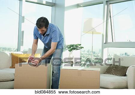 Stock Photography - Caucasian man taping cardboard box in living room. Fotosearch