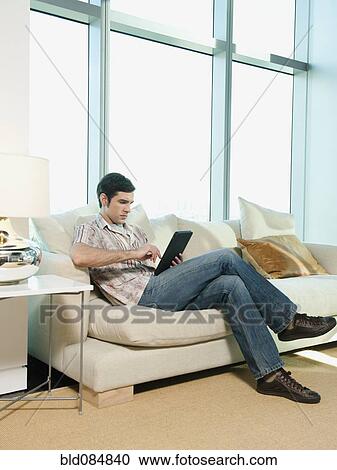 Stock Image - Caucasian man using digital tablet in living room. Fotosearch