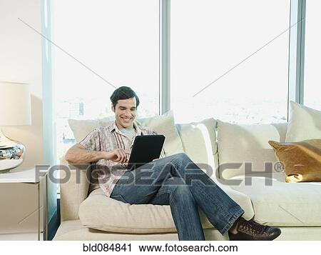 Stock Image - Caucasian man using digital tablet in living room. Fotosearch