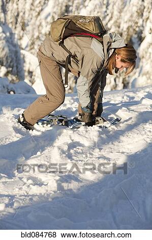 Stock Photo - Caucasian woman fixing snowshoes in snow. Fotosearch