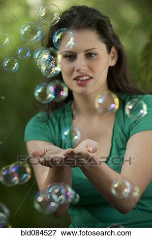 Stock Photo - Caucasian woman trying to catch bubbles in her hands. Fotosearch