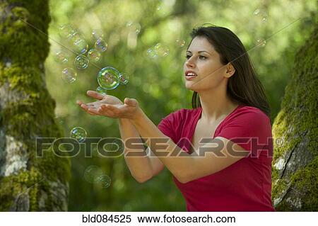 Stock Photography - Caucasian woman trying to catch bubbles in her hands. Fotosearch