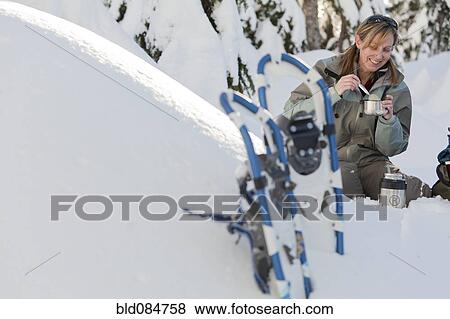 Stock Photo - Caucasian woman with snowshoes eating in snow. Fotosearch