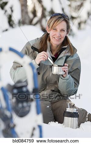Stock Photo - Caucasian woman with snowshoes eating in snow. Fotosearch
