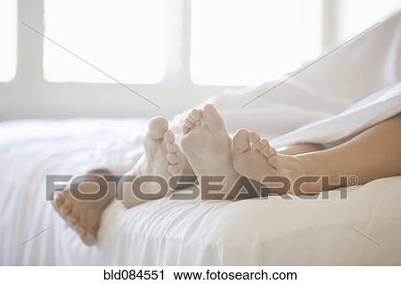 Stock Image - Close up of couple's feet in bed. Fotosearch