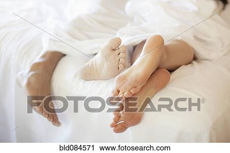 Stock Image - Close up of couple's feet in bed. Fotosearch