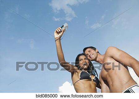 Stock Image - Couple in bathing suits taking self-portrait with digital camera. Fotosearch