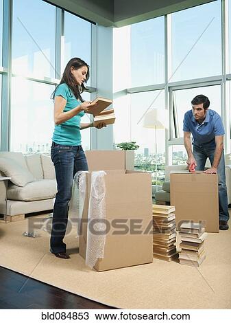 Stock Image - Couple packing boxes in living room. Fotosearch