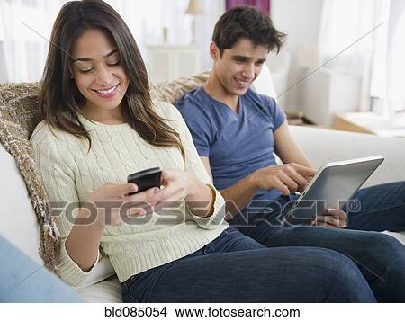 Picture - Couple using technology on sofa together. Fotosearch