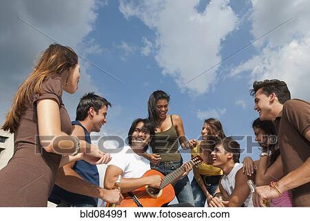 Stock Image - Friends listening to man playing guitar. Fotosearch