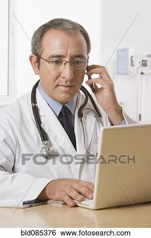 Stock Photograph - Hispanic doctor with laptop talking on cell phone. Fotosearch