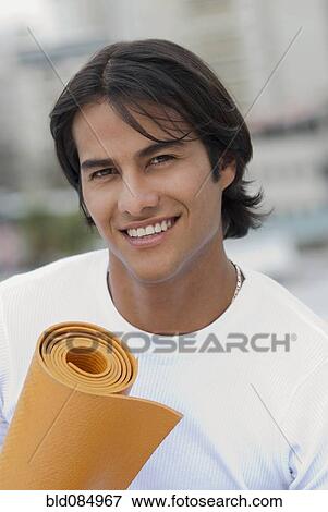 Stock Photo - Hispanic man holding yoga mat. Fotosearch