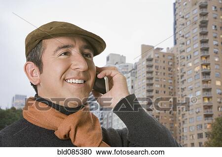 Stock Image - Hispanic man in cap talking on cell phone. Fotosearch