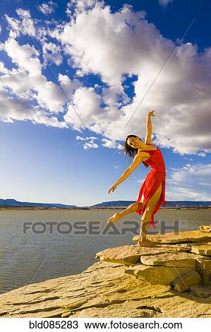 Stock Image - Hispanic woman dancing near lake. Fotosearch