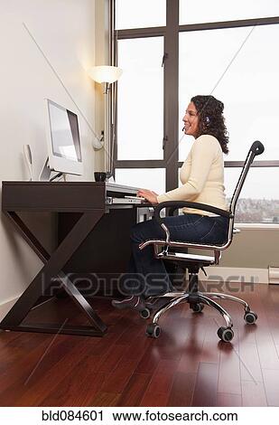 Stock Image - Hispanic woman in headset working on computer. Fotosearch