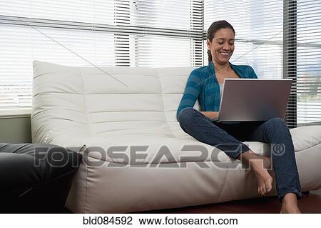 Stock Image - Hispanic woman on sofa using laptop. Fotosearch