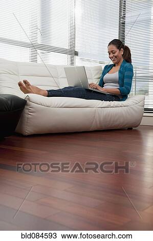Stock Image - Hispanic woman on sofa using laptop. Fotosearch