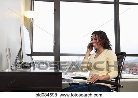 Hispanic woman talking on phone at desk View Large Photo Image Stock Photo - Hispanic woman talking on phone at desk. Fotosearch