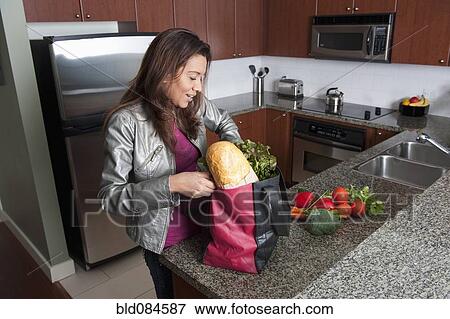 Hispanic woman unloading groceries in kitchen View Large Photo Image Stock Photo - Hispanic woman unloading groceries in kitchen. Fotosearch
