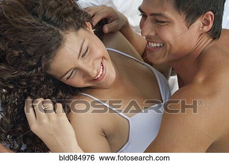 Stock Photograph - Laughing Hispanic couple laying in bed. Fotosearch