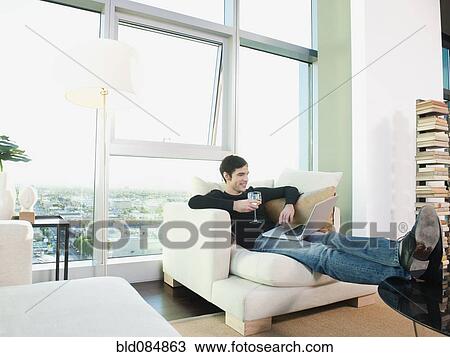 Stock Image - Man drinking wine and using laptop. Fotosearch