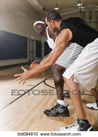 Stock Image - Men playing basketball on basketball court. Fotosearch
