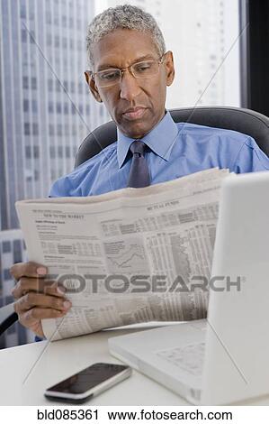 Stock Image - Mixed race businessman reading newspaper at desk. Fotosearch