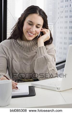 Stock Photo - Mixed race businesswoman talking on cell phone at desk. Fotosearch