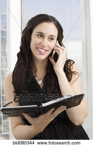 Picture - Mixed race businesswoman with notebook talking on cell phone. Fotosearch