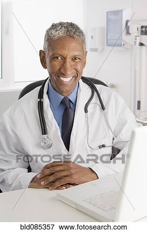 Stock Photo - Mixed race doctor sitting at desk. Fotosearch