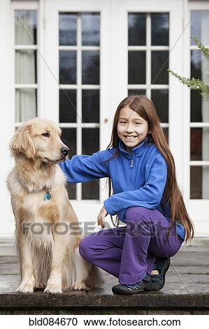 Stock Image - Mixed race girl petting Golden retriever. Fotosearch