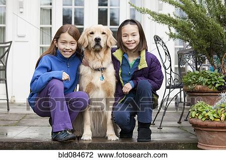 Stock Image - Mixed race girls hugging Golden retriever. Fotosearch