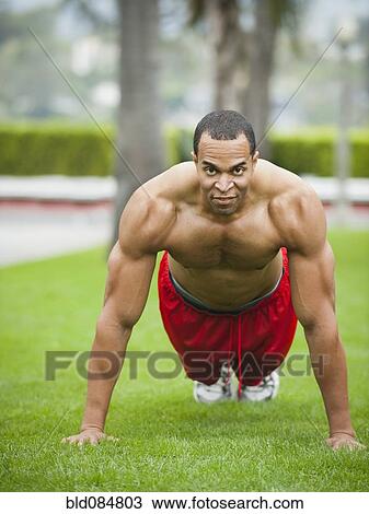 Stock Image - Mixed race man doing push-ups in park. Fotosearch