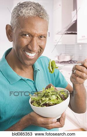 Mixed race man eating salad in kitchen View Large Photo Image Stock Image - Mixed race man eating salad in kitchen. Fotosearch