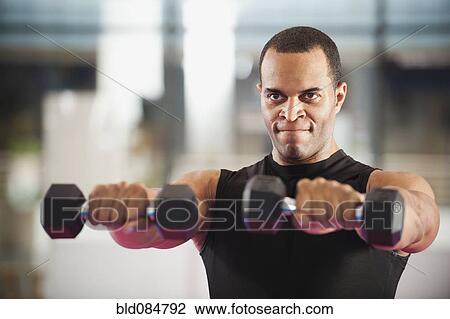 Stock Image - Mixed race man exercising with hand weights in health club. Fotosearch