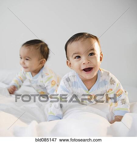 Stock Photo - Mixed race twins crawling on bed. Fotosearch