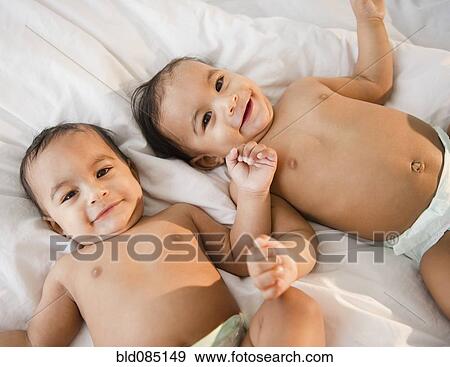 Stock Photo - Mixed race twins in diapers laying on bed. Fotosearch