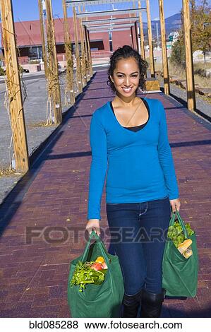 Stock Photo - Mixed race woman carrying groceries in reusable bag. Fotosearch