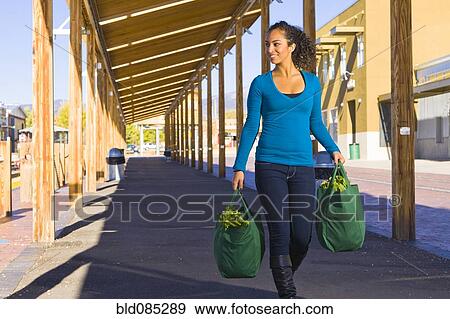 Stock Photo - Mixed race woman carrying groceries in reusable bag. Fotosearch