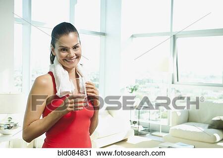 Stock Image - Mixed race woman drinking water in living room. Fotosearch