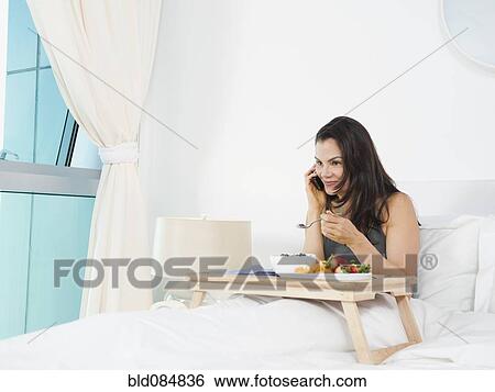 Stock Photograph - Mixed race woman eating breakfast in bed. Fotosearch