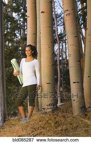 Stock Photo - Mixed race woman holding yoga mat in forest. Fotosearch