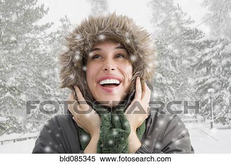 Stock Photography - Mixed race woman in fur hood watching snow fall. Fotosearch