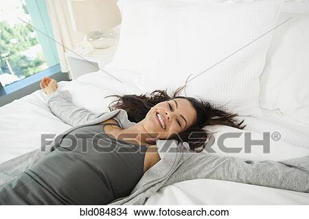 Picture - Mixed race woman laying on bed. Fotosearch