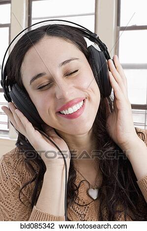 Stock Image - Mixed race woman listening to headphones. Fotosearch