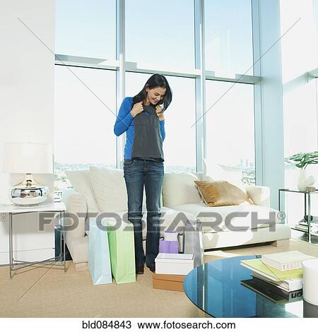 Stock Image - Mixed race woman looking at clothing in living room. Fotosearch