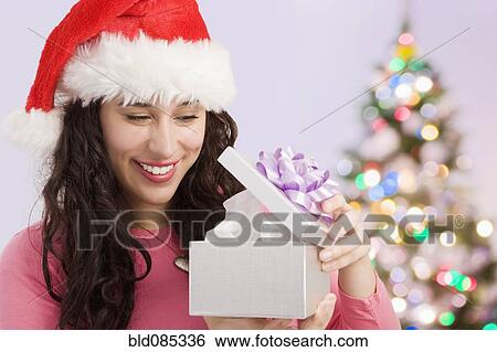 Stock Photograph - Mixed race woman opening Christmas gift. Fotosearch