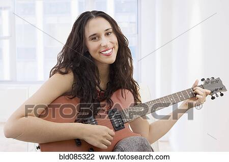 Stock Image - Mixed race woman playing guitar. Fotosearch